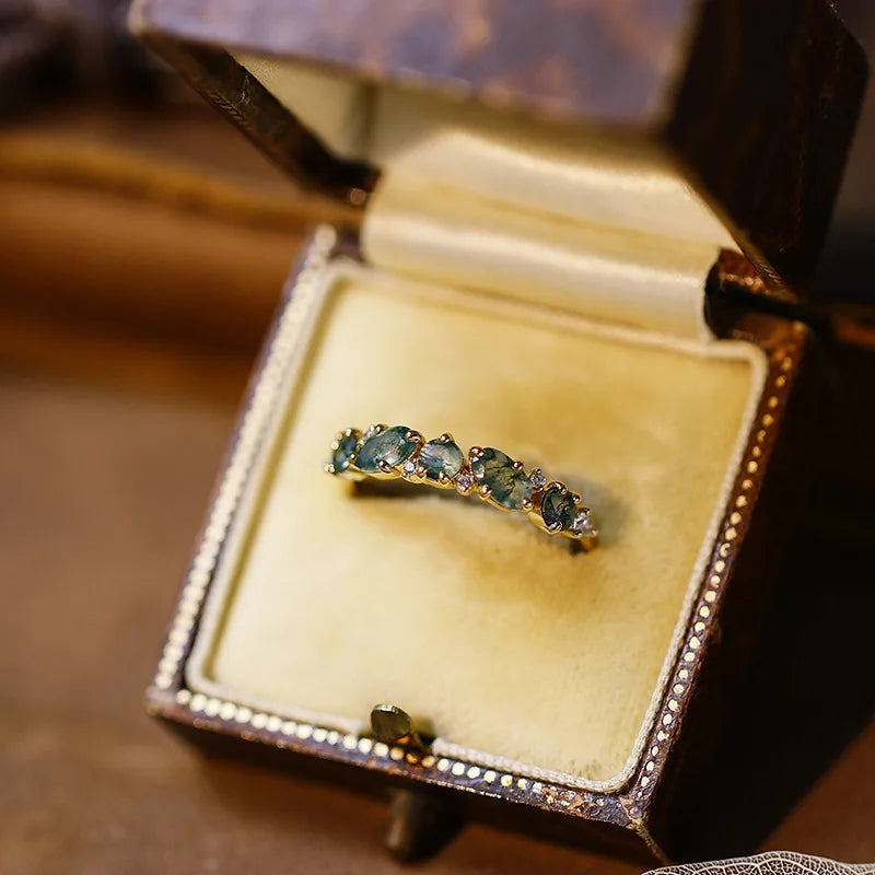Gold ring with green gemstones in an open jewelry box on a wooden surface