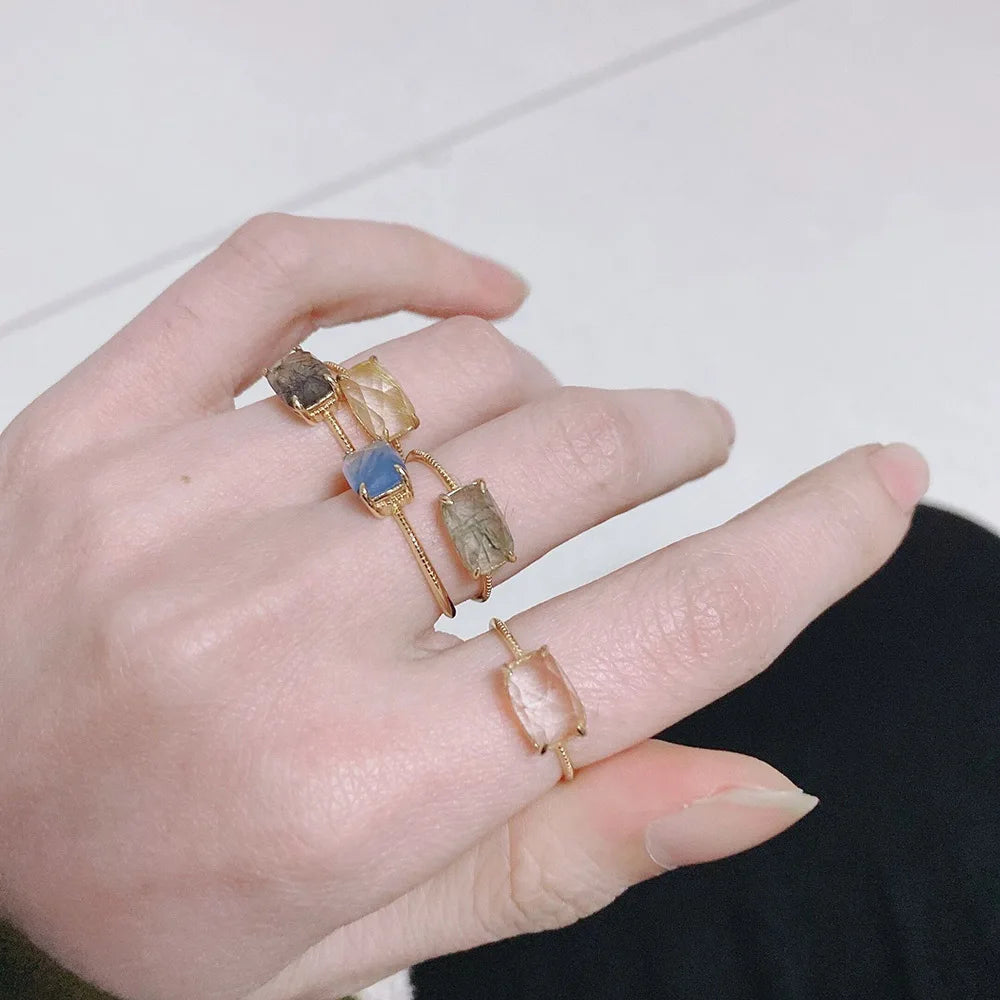 Hand wearing multiple rings with different colored stones on a neutral background