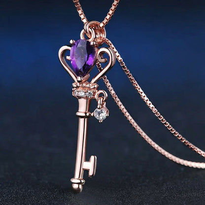 Rose gold key-shaped pendant with purple gemstone on a dark background.