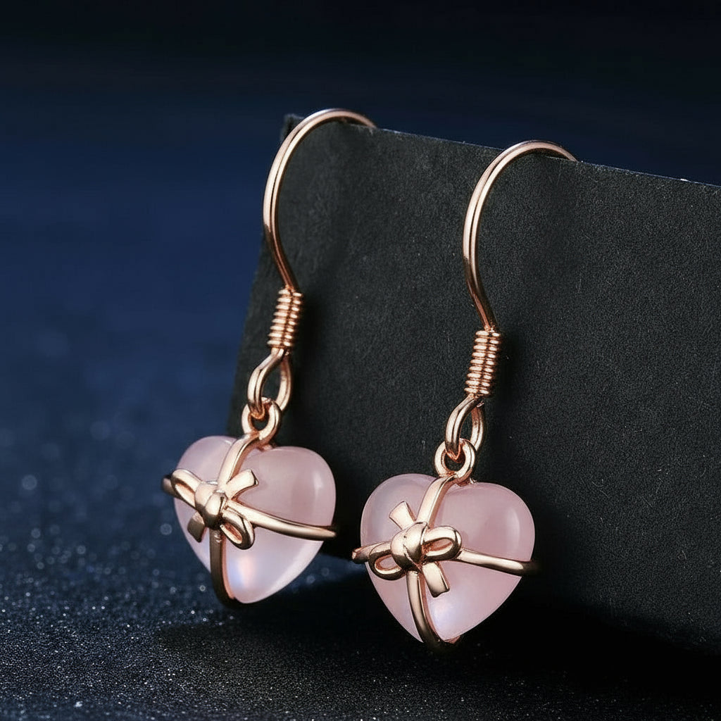 Rose gold heart-shaped earrings with bow design on a dark background.