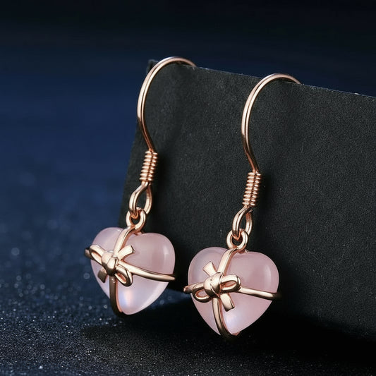 Rose gold heart-shaped earrings with bow design on a dark background.