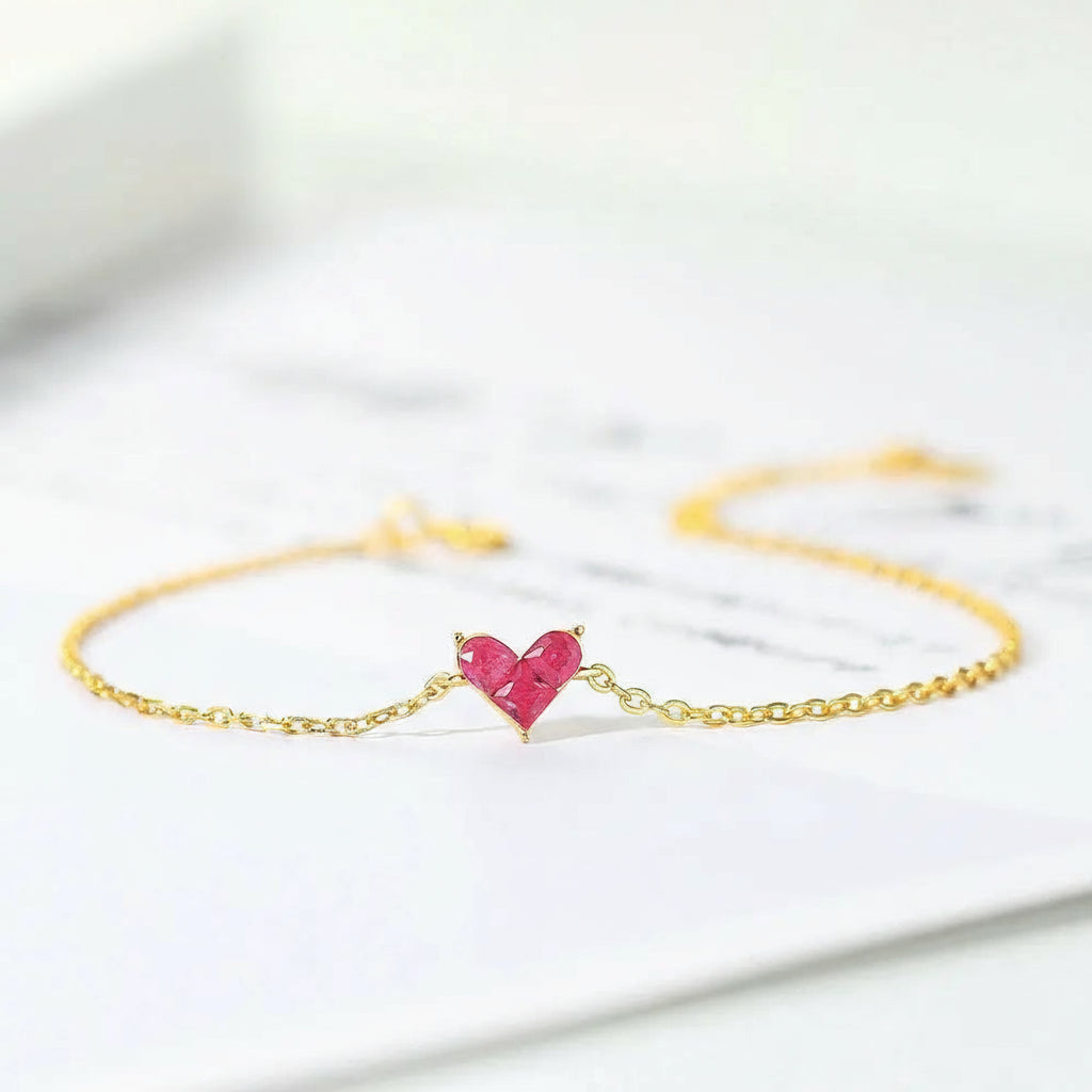 Gold bracelet with a pink heart-shaped gemstone on a light background.