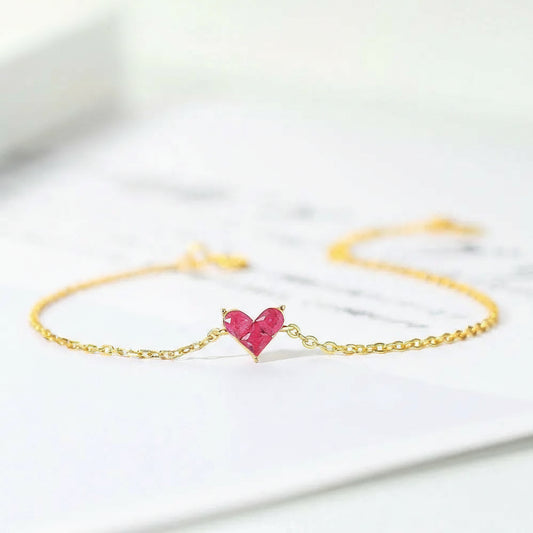 Gold bracelet with a pink heart-shaped gemstone on a light background.