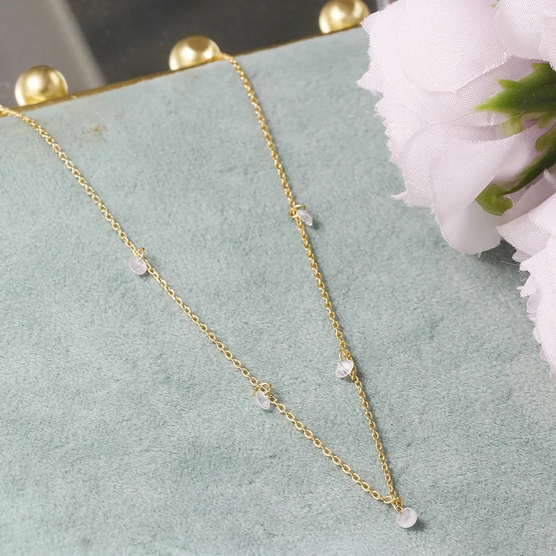925 silver necklace with small beads on a light green surface with flowers in the background