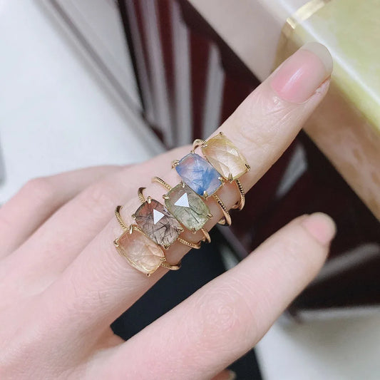 Hand wearing a stack of gold rings with multicolored gemstones.