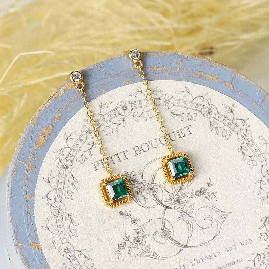 Green emerald drop earrings displayed on decorative box