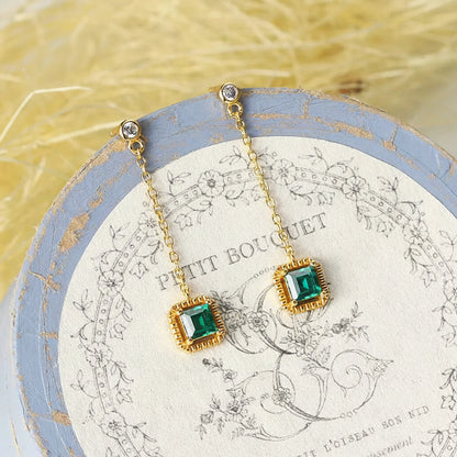 Green emerald drop earrings displayed on decorative box