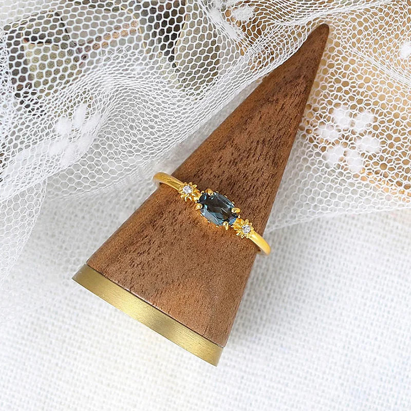 Gold ring with a blue topaz gemstone on a wooden stand against a white lace background