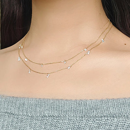 Silver necklace with small pendants on a person wearing a light blue sweater.