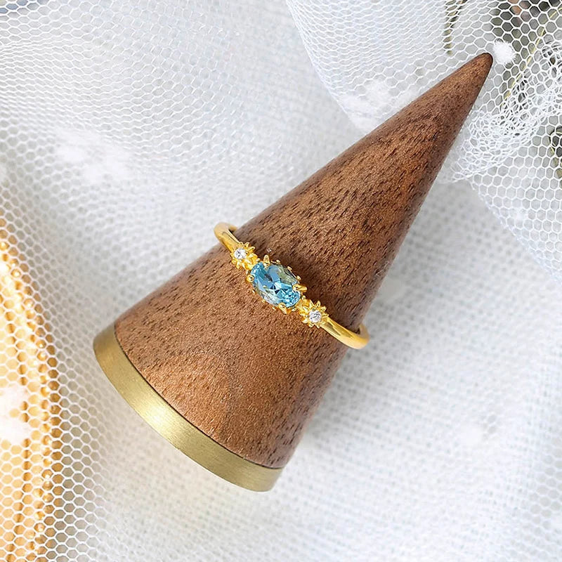 Gold ring with a blue gemstone on a wooden cone against a white background