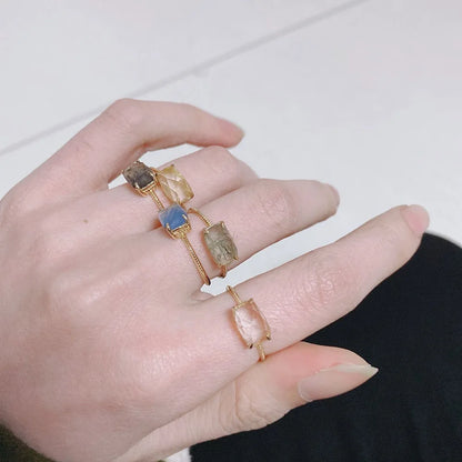 Hand wearing multiple rings with natural stone designs on a neutral background