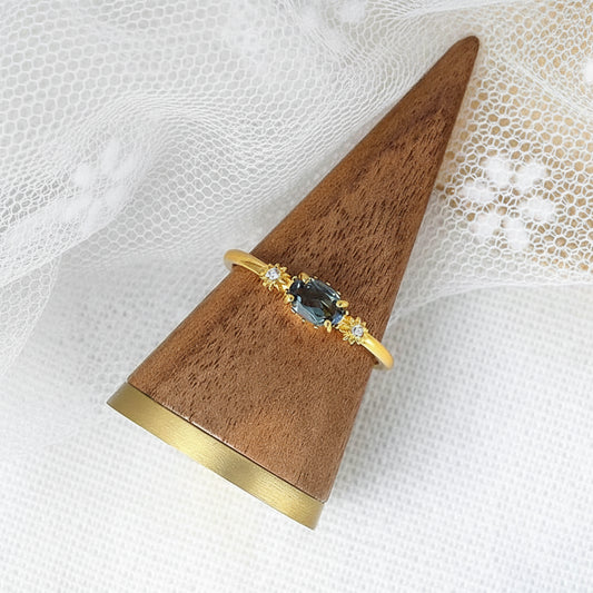 Gold ring with a blue gemstone on a wooden stand against a white lace background