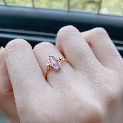 Rose gold ring with a pink gemstone on a person's finger, blurred background